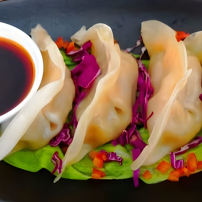 Thai dumplings with red cabbage, bell peppers, and a side of soy sauce.