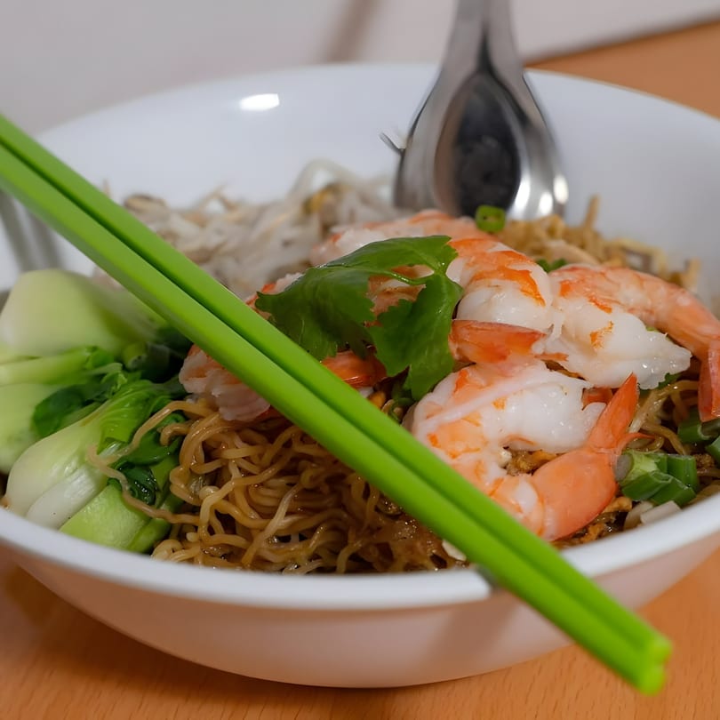 Ninethai Kitchen's shrimp and noodle dish with bok choy, bean sprouts, and green chopsticks.