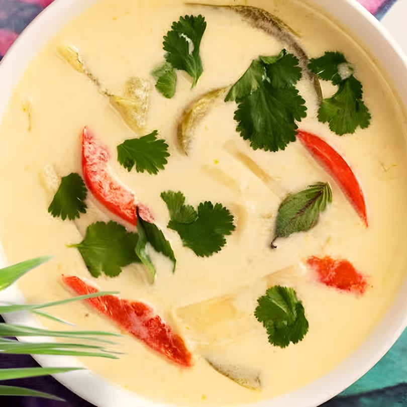 Creamy Thai soup with red chili, green herbs, and other ingredients in a white bowl.